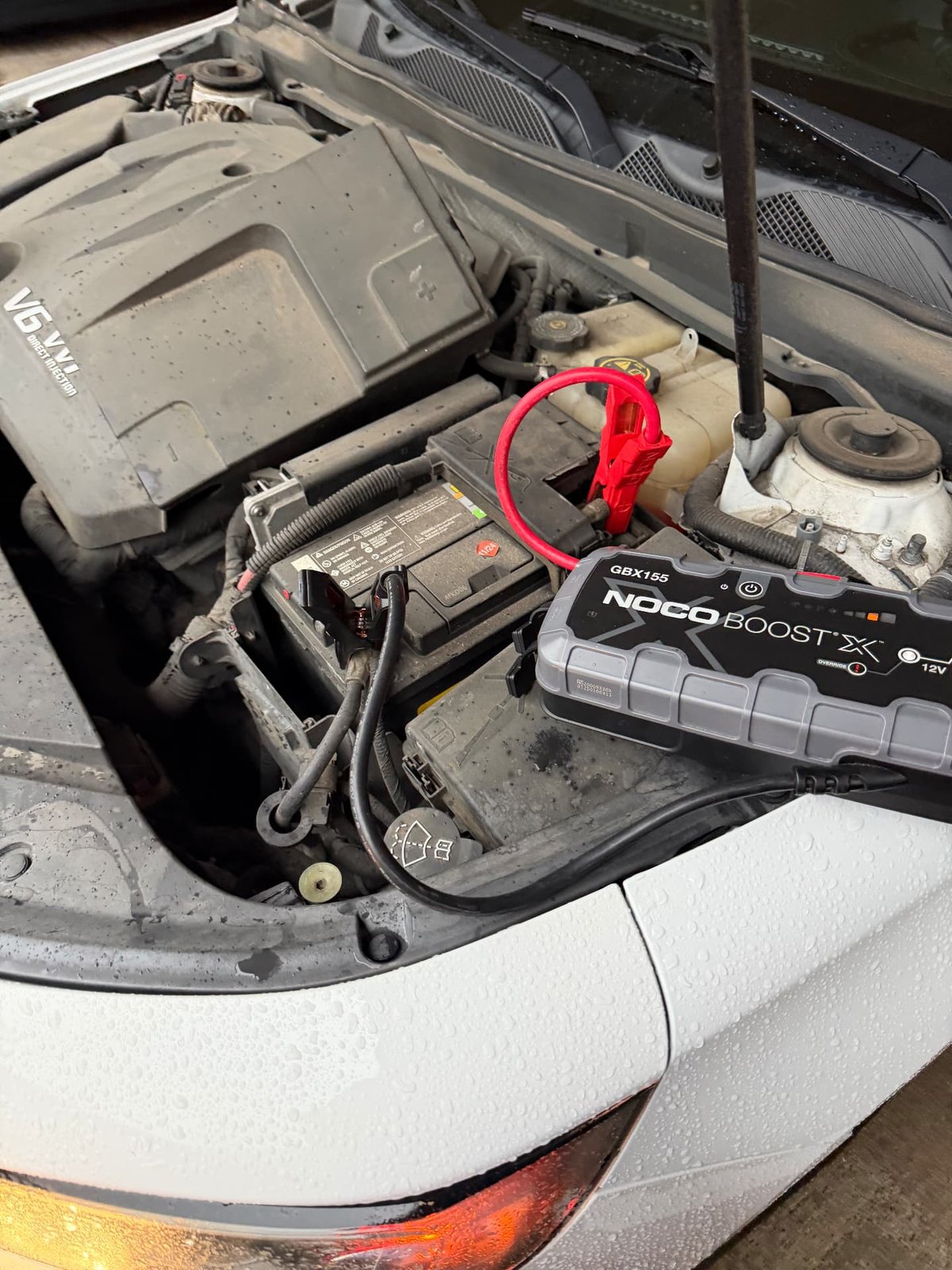 NOCO Boost X GBX155 connected to an under-hood 12V battery in a white V6 vehicle during a mobile jump start by All Hours Roadside