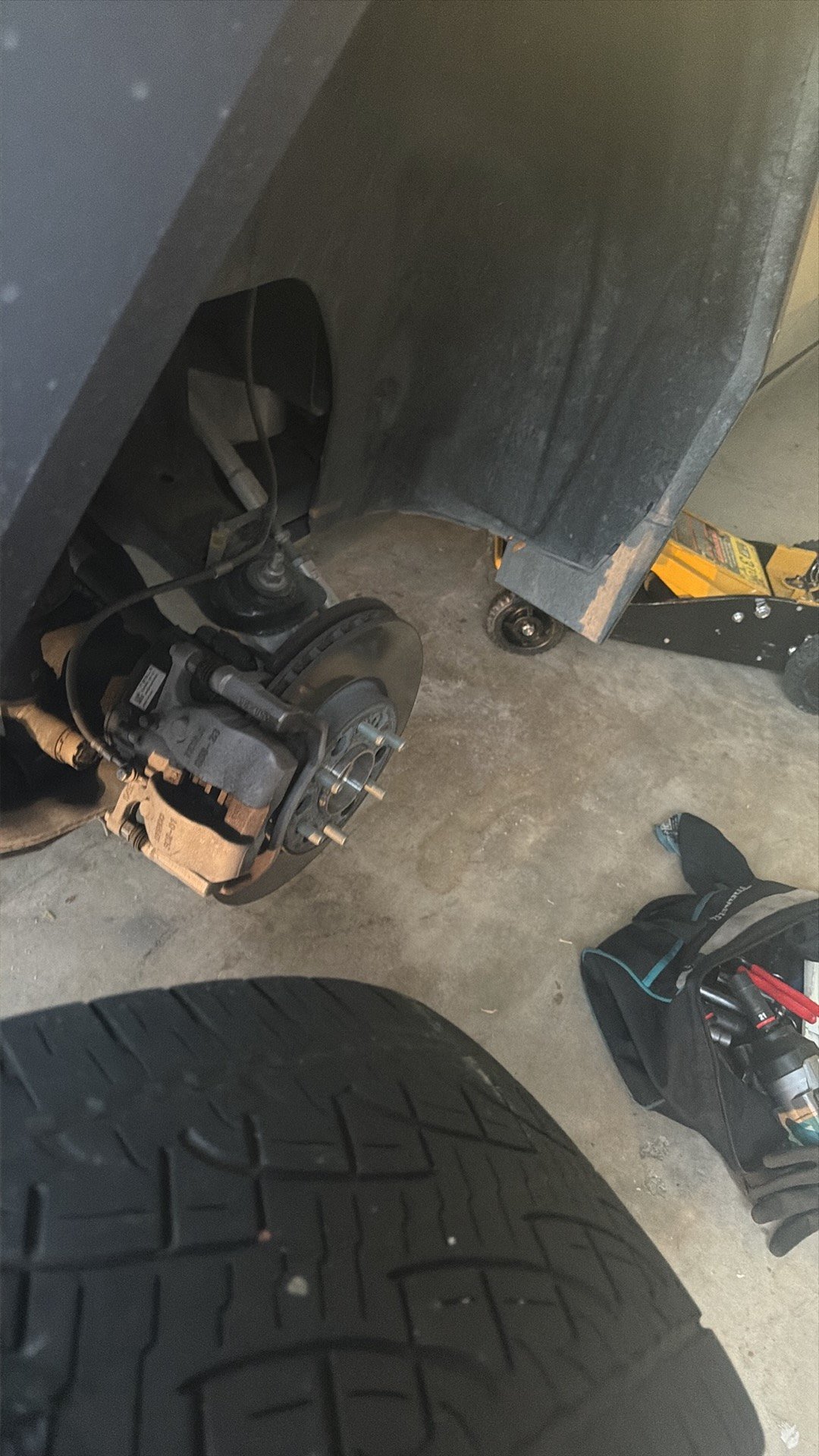 Close view of a Cybertruck wheel well with wheel removed, brake disc and caliper visible, tire and tools on the garage floor