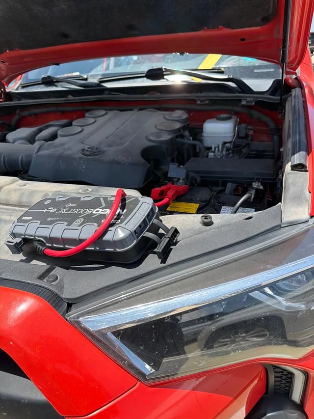 NOCO Boost X lithium jump pack clamped to a modern 12V vehicle battery during an ECU-safe mobile jump start in the DFW metro — All Hours Roadside