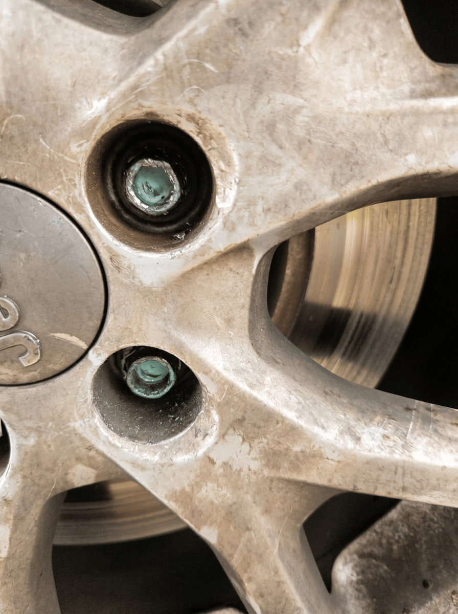 Two heavily corroded aluminum lug nuts seized deep inside a Jeep alloy wheel with brake rotor visible through the spokes — mobile stripped-lug extraction by All Hours Roadside in the Dallas–Fort Worth metro