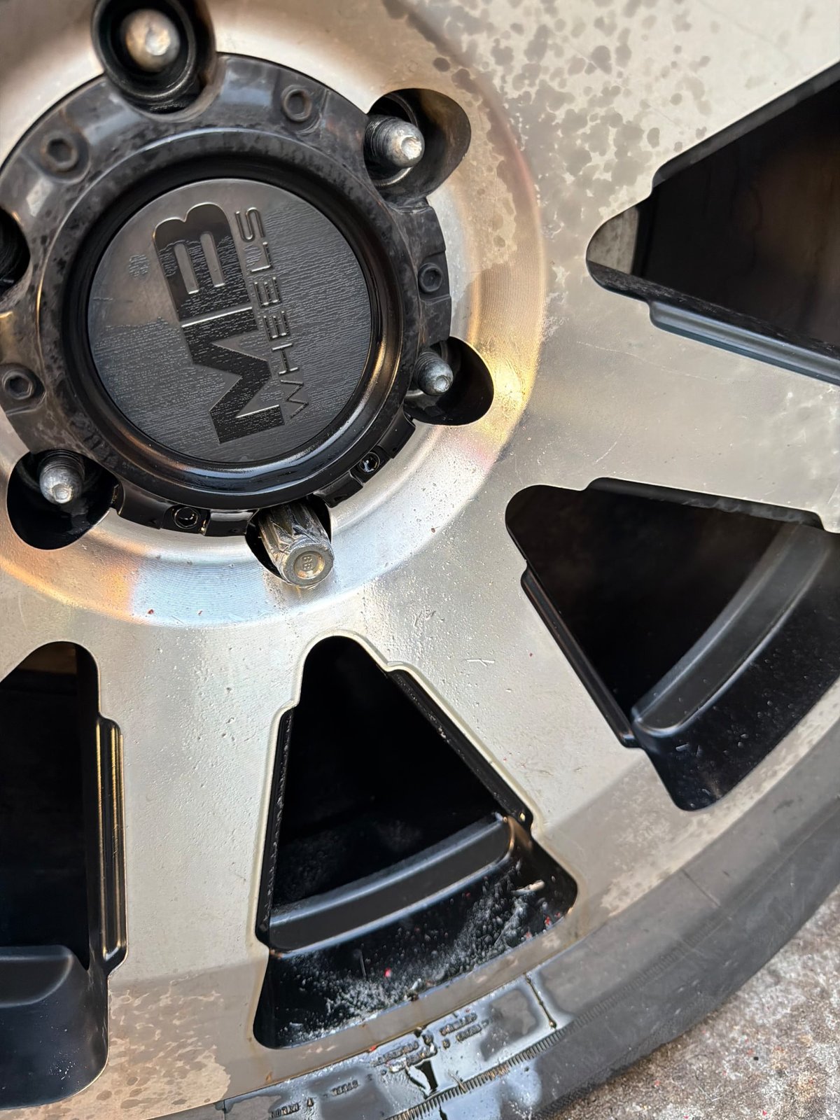 Close-up of a black KMC XD Series wheel on a GMC Sierra showing a spline-drive locking lug nut with the key missing — removed on-site by All Hours Roadside in DFW