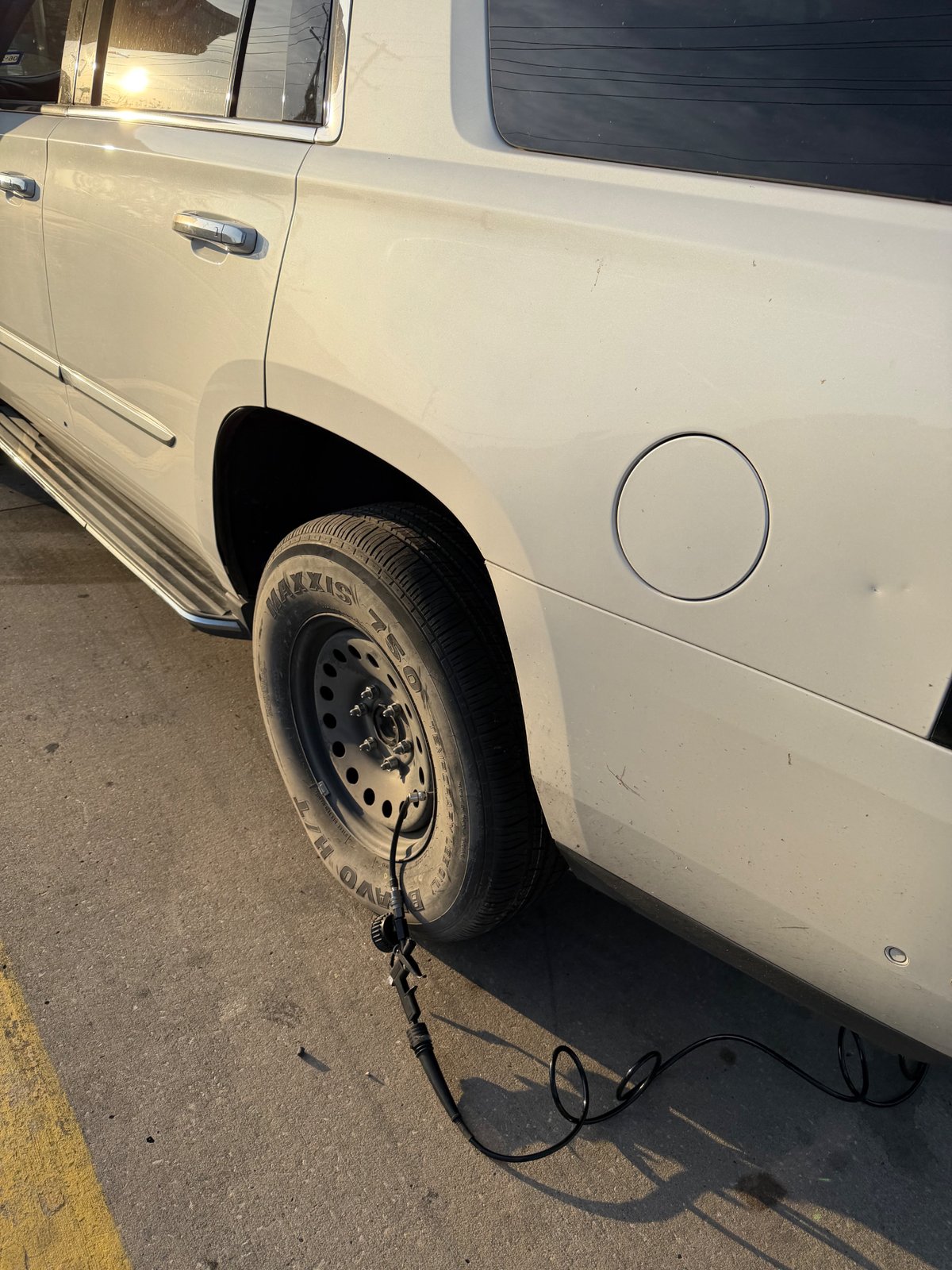 Mobile spare tire change and inflation in Grapevine, TX — parking-lot service, no tow required All Hours Roadside spare tire change on a white Cadillac Escalade in a Grapevine, TX parking lot — full-size spare mounted on the rear passenger side, portable 12V inflator topping off tire pressure roadside.