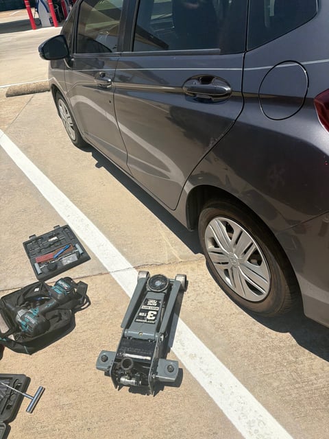 Gray Honda Fit at a Plano TX fuel-station lot with Pittsburgh 3-ton rapid-pump floor jack and tire plug kit staged next to the rear wheel — All Hours Roadside mobile tire repair