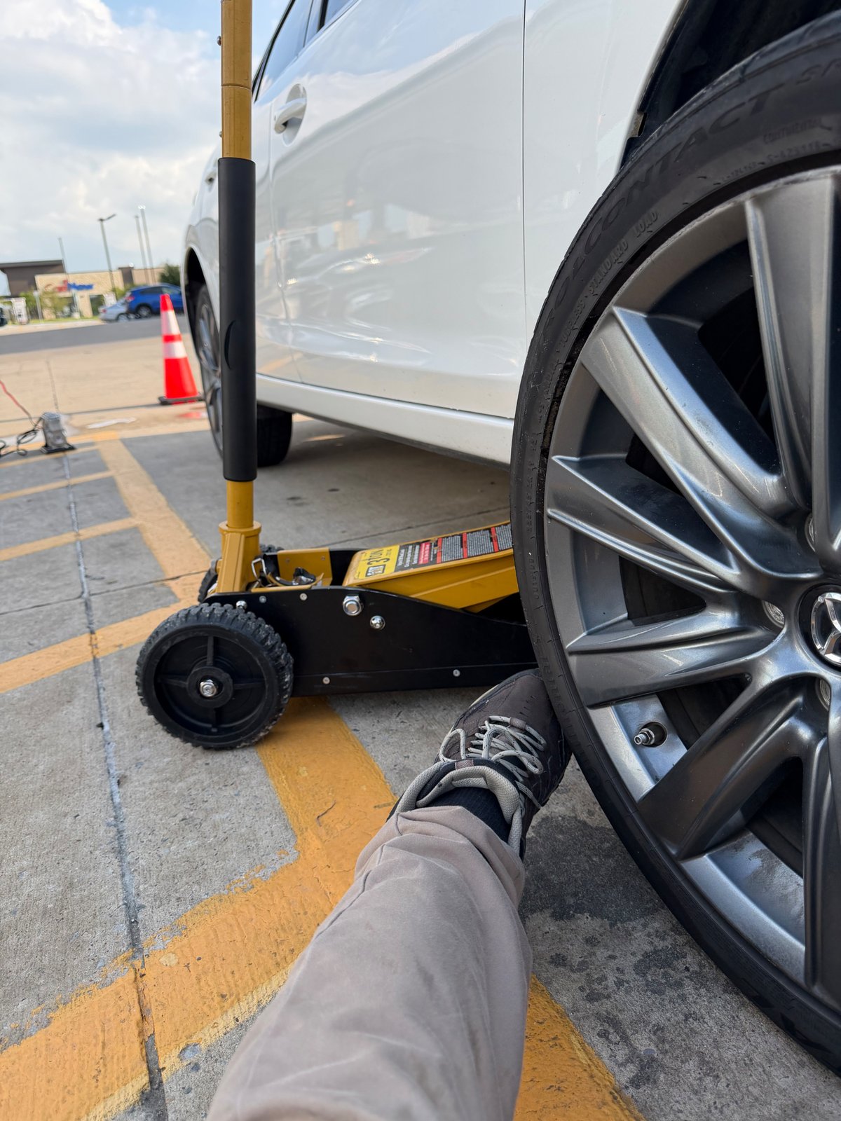 Mercedes sedan lifted on a 3-ton floor jack with a safety cone deployed in a DFW retail parking lot during a mobile tire change
