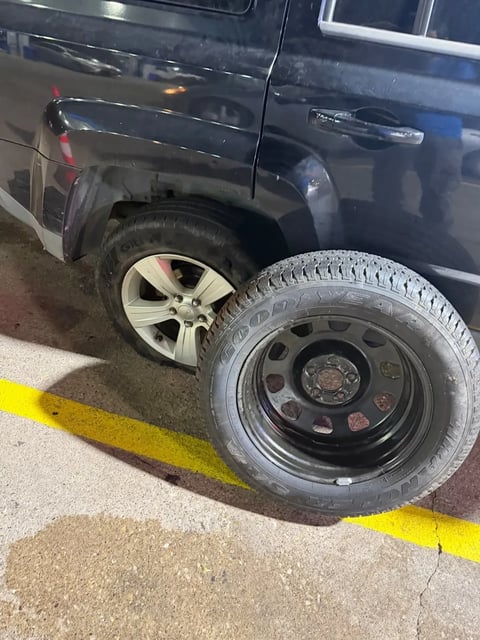 Goodyear spare tire on a black steel wheel beside a dark SUV before a roadside tire change