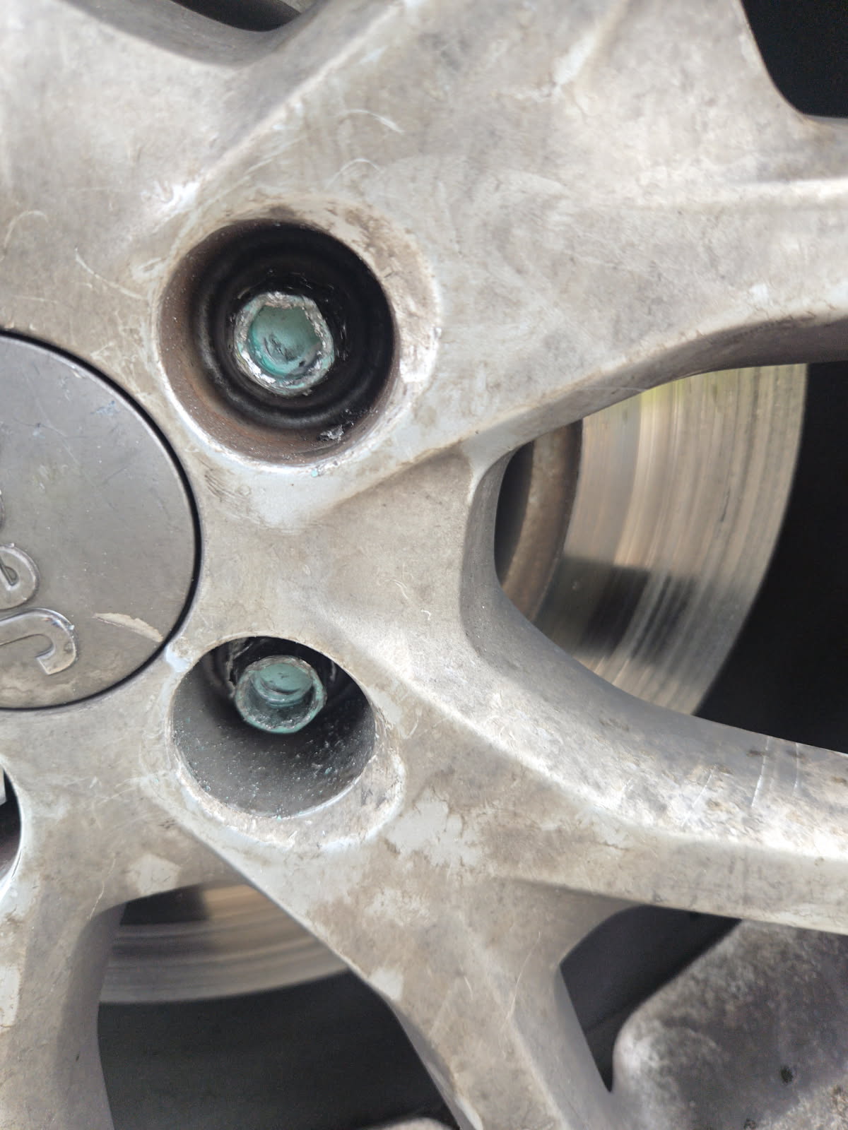 Two corroded, green-oxidized stripped lug nuts seated inside a multi-spoke aluminum alloy wheel — both extracted on-site by All Hours Roadside in the Dallas–Fort Worth metro