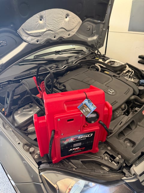 JNC950 12V professional jump pack clamped to a dead OEM battery on a Mercedes-Benz V6 during a roadside jump start in a Frisco TX garage — All Hours Roadside mobile battery boost