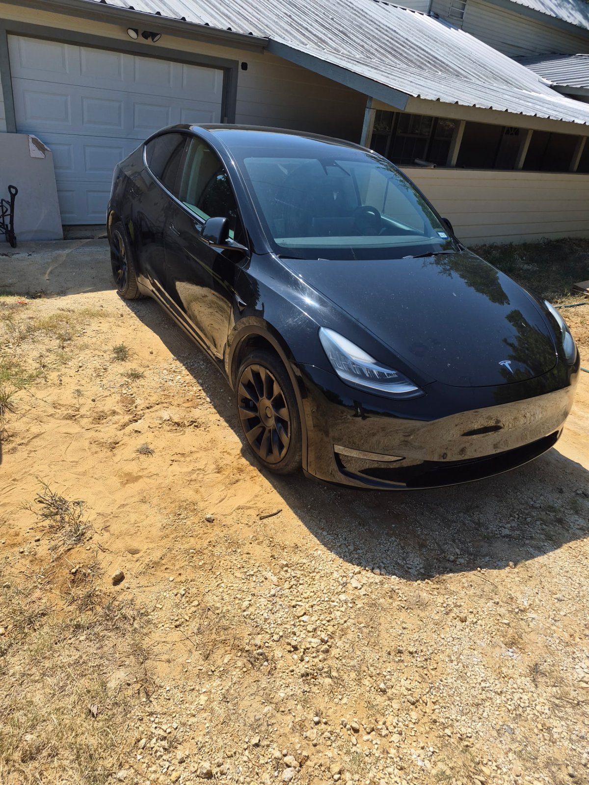 Black Tesla Model Y fully lowered and sitting on a gravel driveway in front of a house after a completed mobile tire change in DFW Black Tesla Model Y fully lowered and sitting on a gravel driveway in front of a house after a completed mobile tire change in DFW