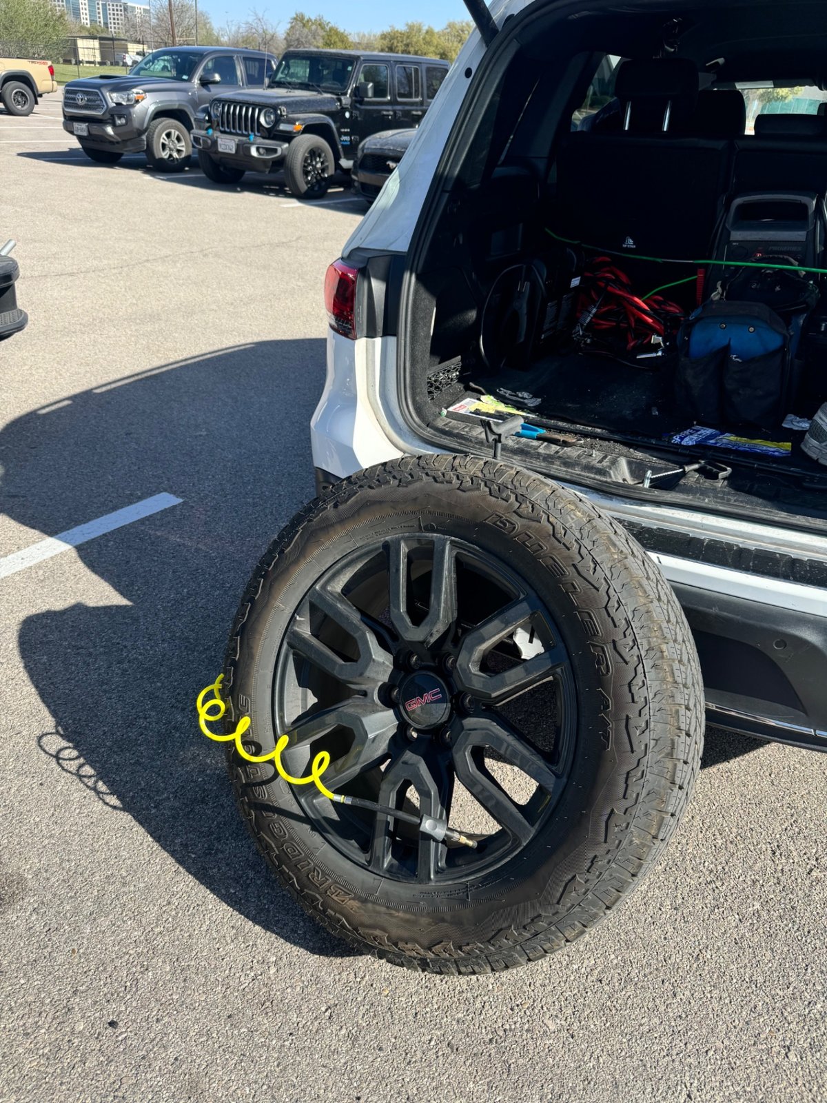 GMC pickup spare tire mounted and being aired up with a coil hose by an All Hours Roadside technician in a DFW parking lot