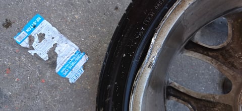 Heavy curb rash and gouging on a multi-spoke aluminum alloy wheel next to a torn ST205/75R15 tire label — inspected by All Hours Roadside in the Dallas–Fort Worth metro