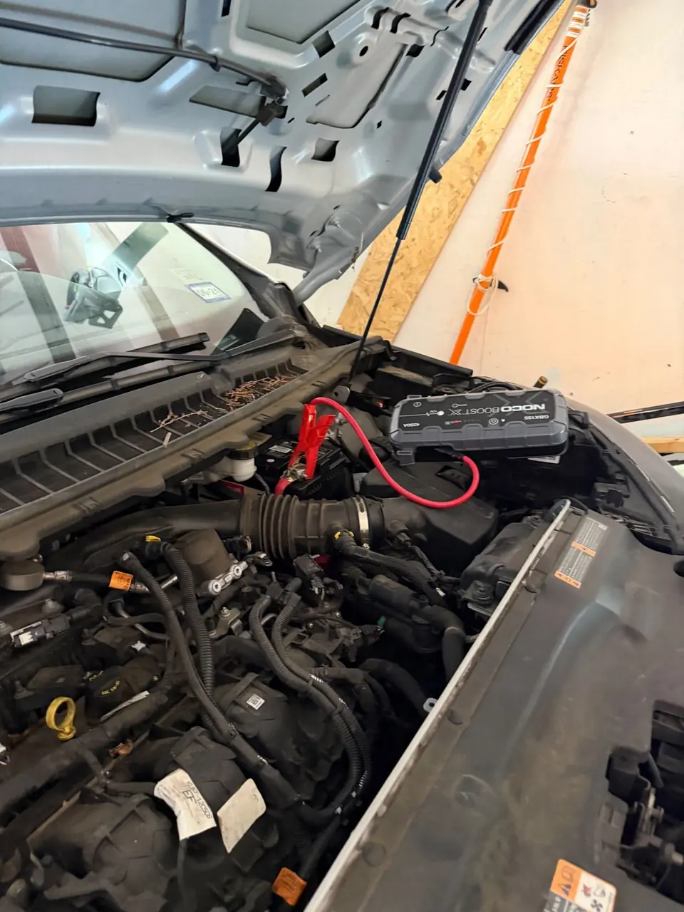 NOCO Boost X portable jump starter clamped to a 12V truck battery under the hood during a roadside jump start in DFW